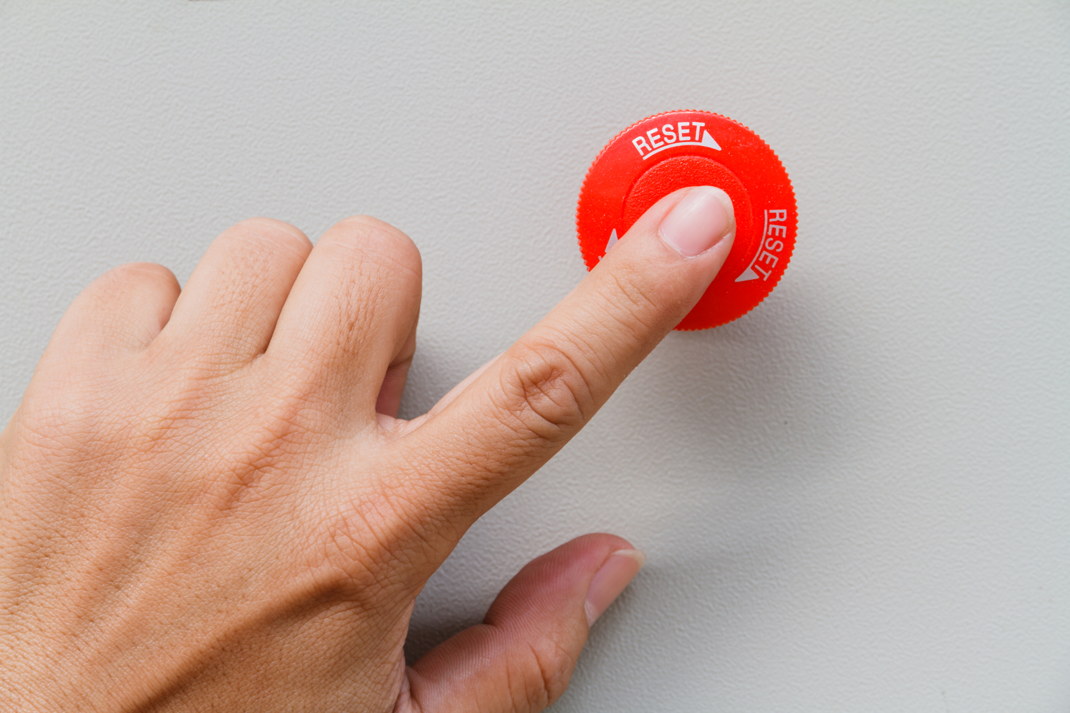 Finger touching a red switch that says “reset” for machine control