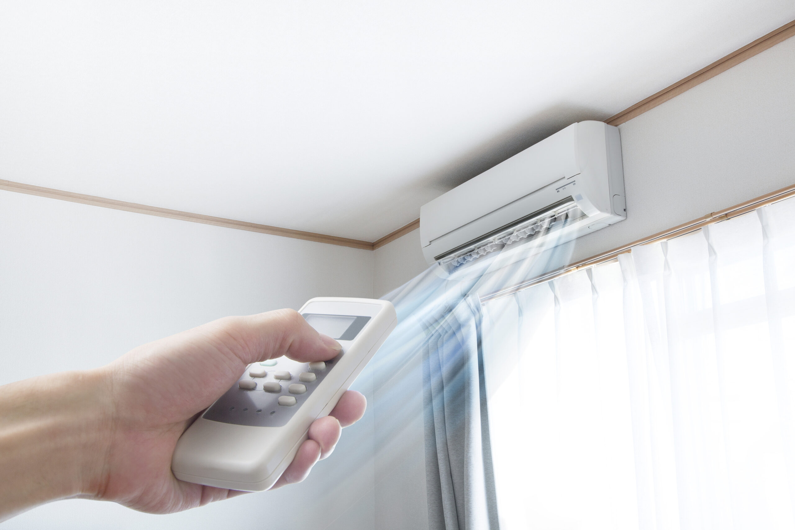 A woman’s hand pointing a remote toward a ductless mini-split that is blowing air