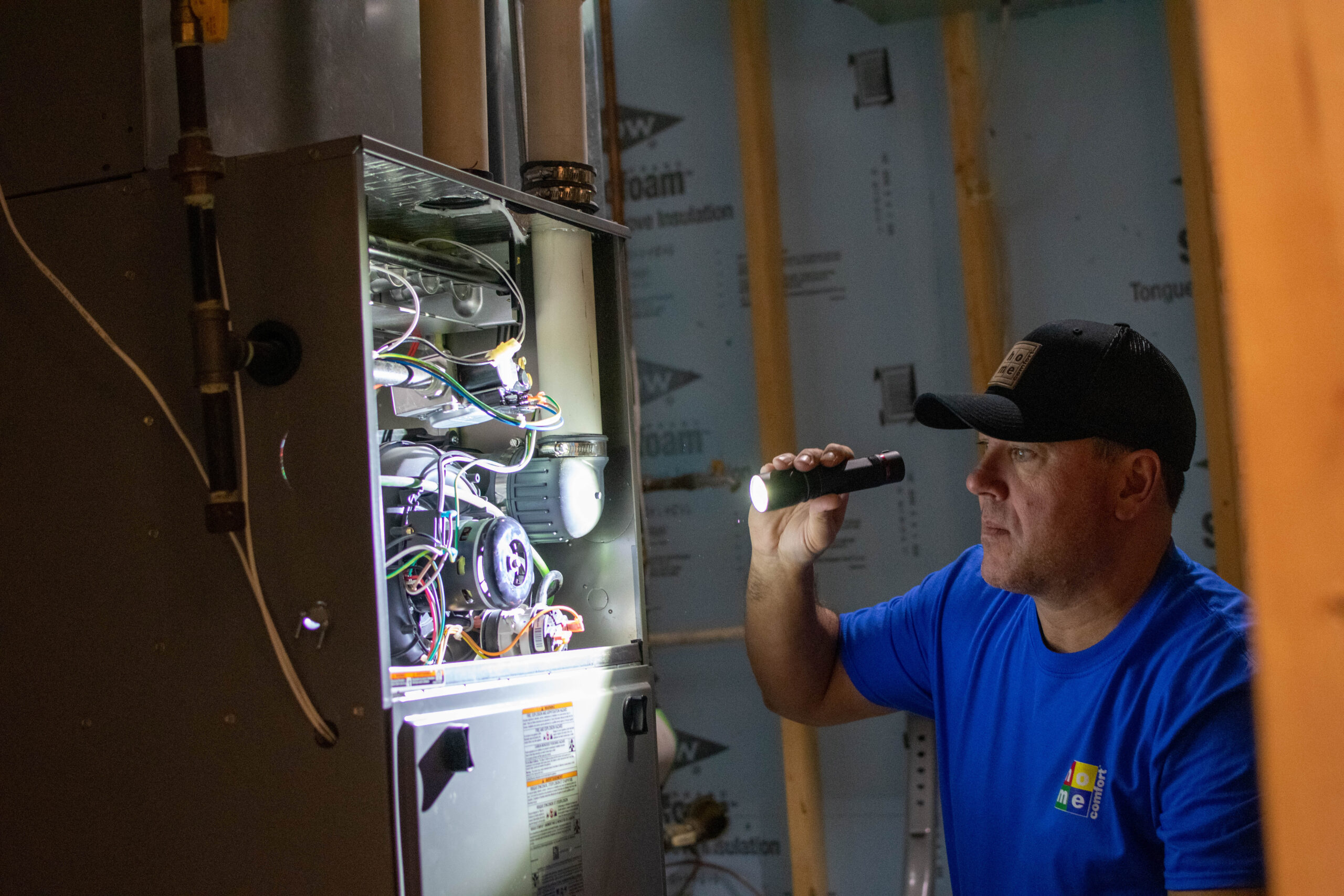 Home Comfort technician checking a home’s furnace with a flashlight