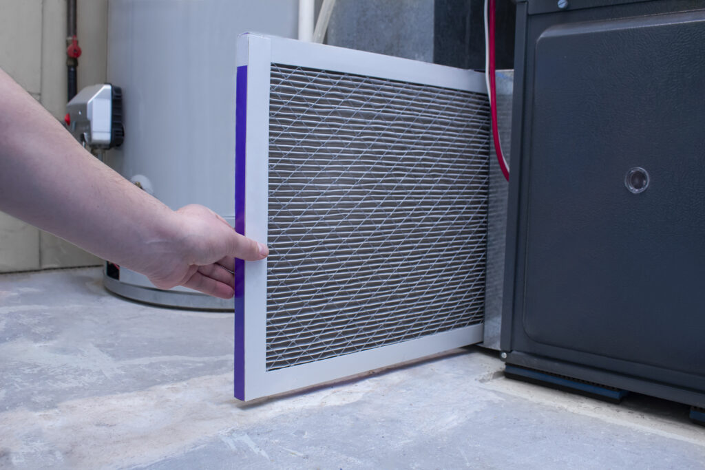 Hand pulling a clogged furnace filter from the unit